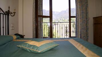 Un dormitorio con cama, mesita de noche, cómoda y balcón con vistas a montañas.