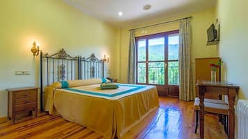 Un dormitorio con cama, mesita de noche, escritorio, silla, ventana con vistas y radiador.