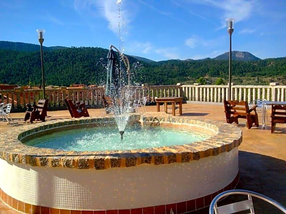 Una piscina circular con una fuente en el centro, rodeada de sillas de descanso y vistas a un paisaje montañoso.