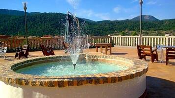 Una piscina circular con una fuente en el centro, rodeada de sillas de descanso y vistas a un paisaje montañoso.