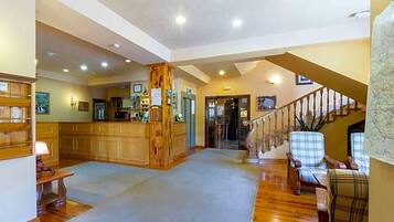 Un vestíbulo amplio con suelo de madera, un mostrador de recepción, una escalera y una zona de estar con sillas a cuadros.