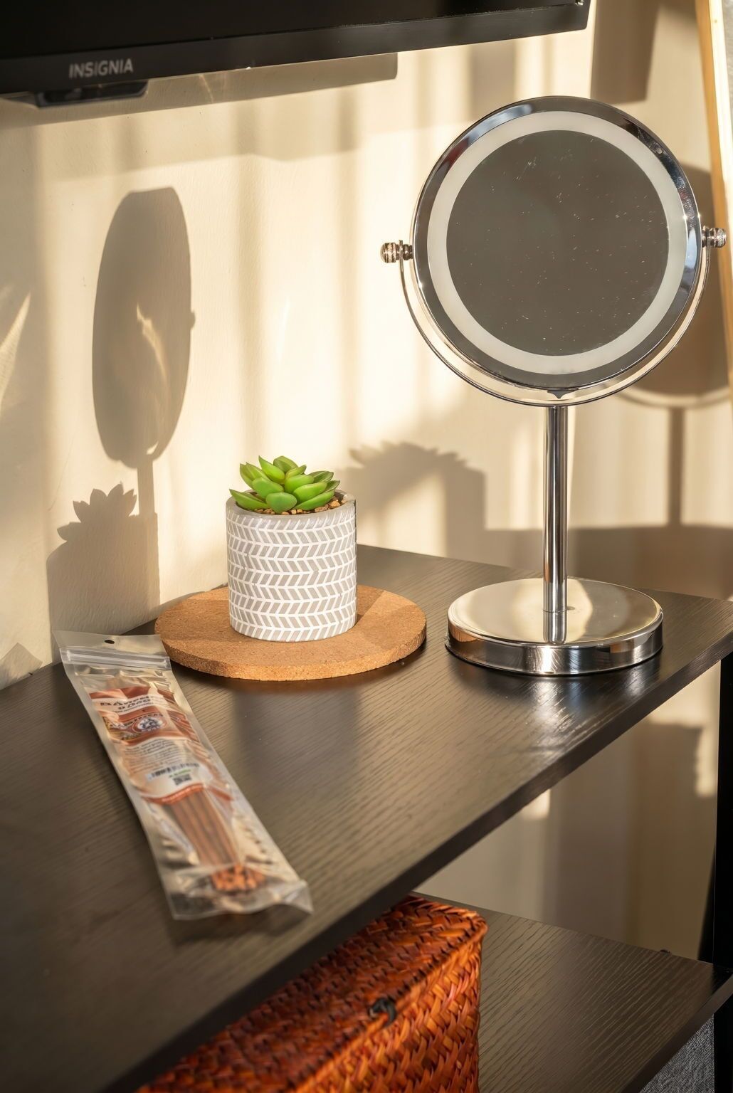 Une coiffeuse avec un miroir rond, un récipient décoré, une petite plante en pot et une boîte de mouchoirs.