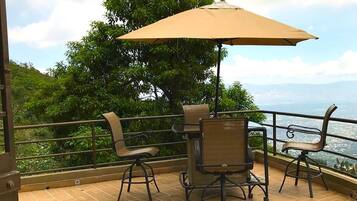 Une terrasse extérieure avec une table et des chaises, un grand parasol et une vue sur la mer.