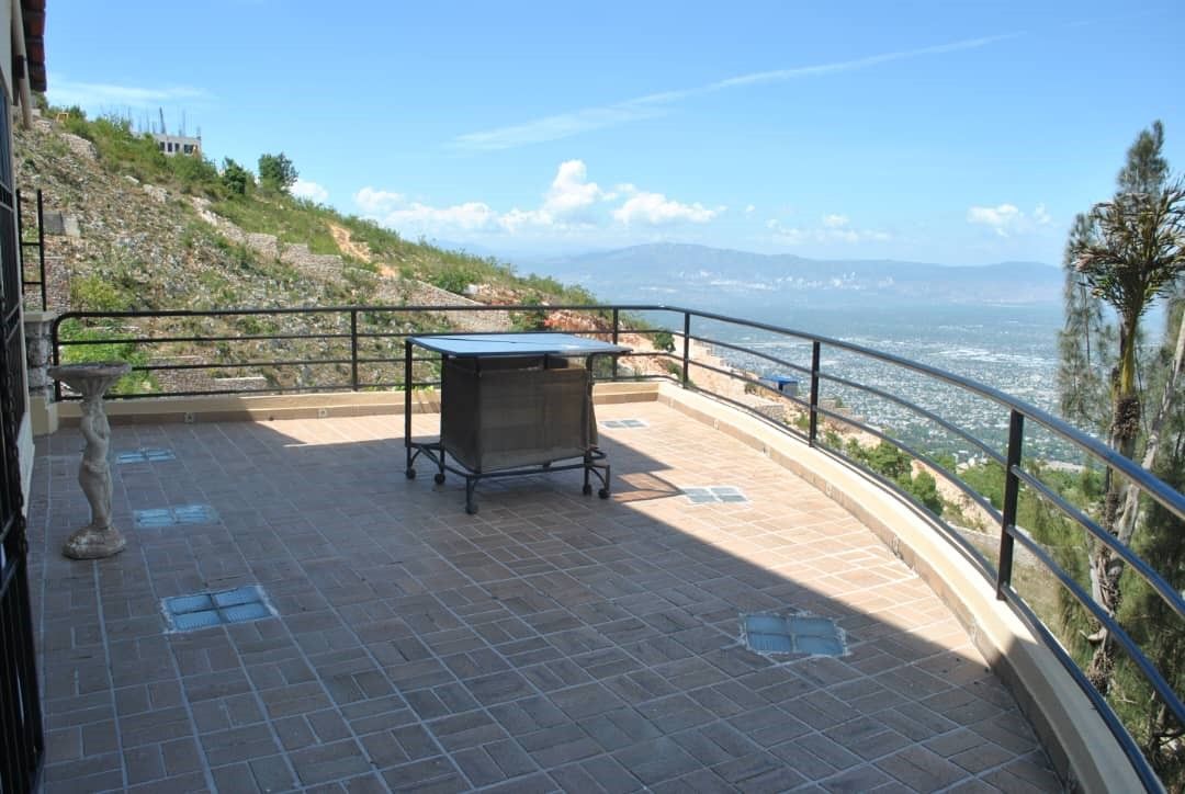 Una terrazza con tavolo e sedie, vista su un paesaggio costiero sotto un cielo sereno.