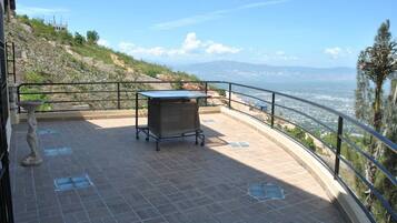 Una terrazza con tavolo e sedie, vista su un paesaggio costiero sotto un cielo sereno.