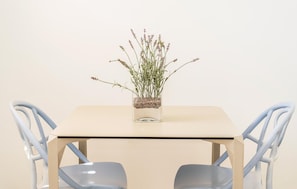 A table with a clear glass vase containing a plant, two chairs with a simple design, and a plain wall in the background. - ISA Marina Riva Le Nuove Dune (Porto Cesareo)
