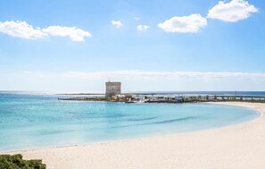 A beach with a clear sky, a sandy shore, and a pier extending into the water. - ISA Marina Riva Le Nuove Dune (Porto Cesareo)