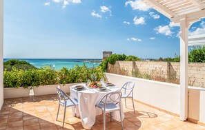 A terrace with a table set for dining, overlooking a coastal view with a clear sky. - ISA Marina Riva Le Nuove Dune (Porto Cesareo)