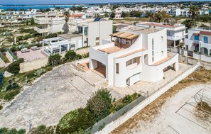 A modern residential building with a flat roof, large windows, and a courtyard with seating. - ISA Marina Riva Le Nuove Dune (Porto Cesareo)