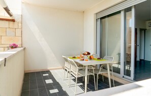 Ein Balkon mit Frühstückstisch, Stühlen, einem Blumentopf und einer Glasschiebetür zu einem Innenraum.