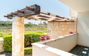 Ein von Steinen gepflasterter Außenbereich mit einer Pergola, einer Steinmauer und einem Blumenbeet.