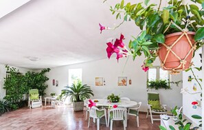 A spacious room with a dining area, several potted plants, and a hanging planter with flowers. - Cozy home in S. Maria del Focallo with WiFi (S. Maria del Focallo)