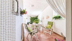 Une pièce aux murs blancs, avec un sol carrelé, une table ronde entourée de chaises et des plantes en pot.