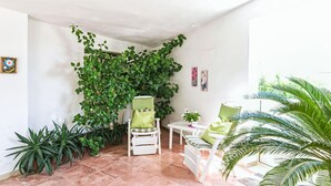 Une pièce avec un mur recouvert de feuilles vertes, une chaise blanche avec un coussin vert, une petite table blanche et une plante en pot.