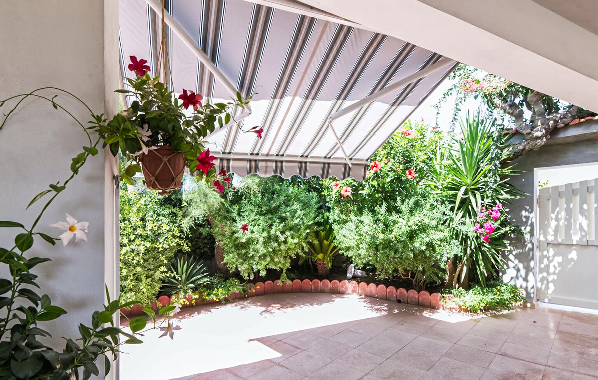 A greenhouse with various plants and flowers, a tiled floor, and a glass ceiling.