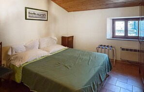 A bedroom with a bed, a radiator, a window, and a framed picture on the wall.