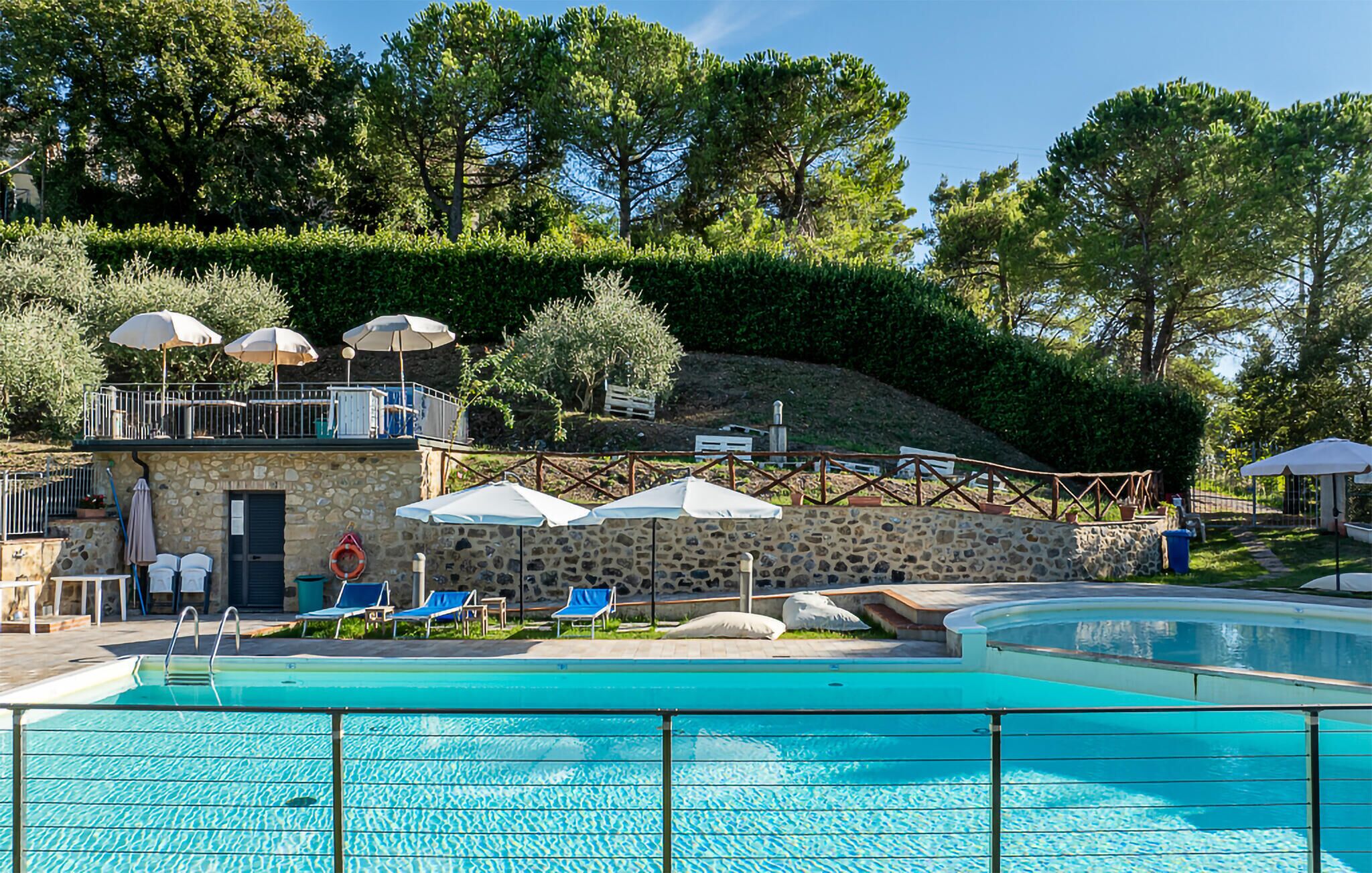 Ein Swimmingpool mit Liegestühlen und Sonnenschirmen, umgeben von Steinmauern und Bäumen.