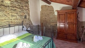 Una camera da letto con una parete in pietra, un armadio in legno, una struttura letto in metallo e una coperta verde.