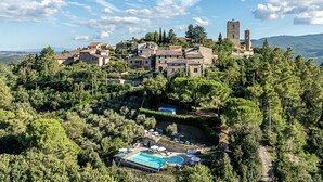 Un borgo collinare con edifici in pietra, una chiesa e una piscina con lettini.