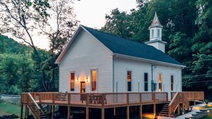 A white building with a green roof, a wooden deck, and a small tower. - Corton Lodge – Riverfront Wedding & Group Retreat (Clendenin)