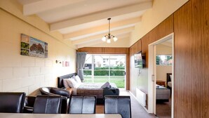 A bedroom with a bed, a table, and chairs, a window with curtains, and a view of the outside.