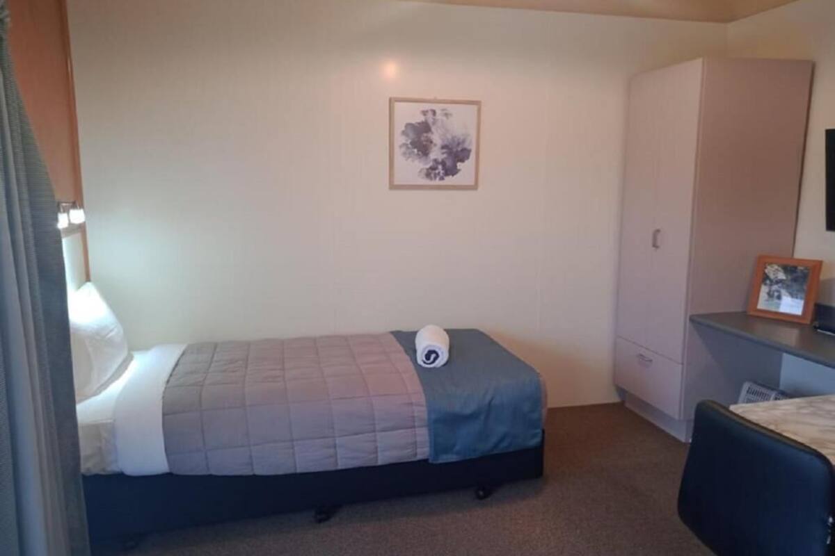 Un dormitorio pequeño y ordenado con cama, escritorio, silla, armario y un cuadro enmarcado en la pared.