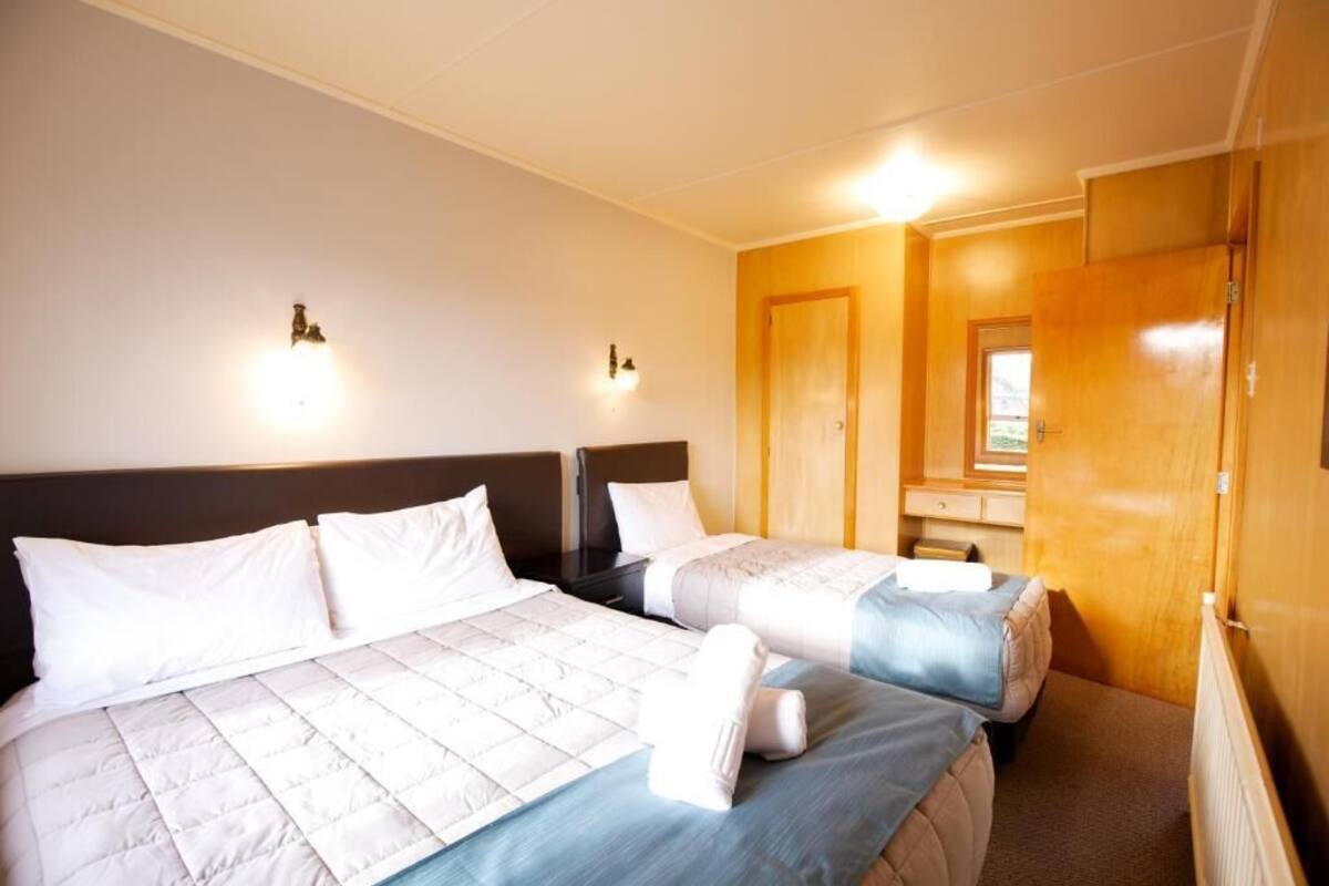 Una habitación de hotel con dos camas, un armario de madera y un escritorio pequeño.