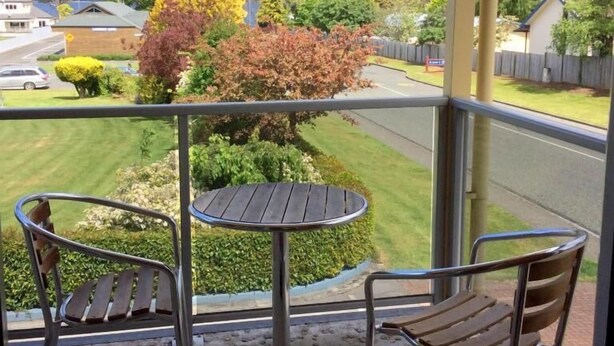 A balcony with two chairs and a small table, overlooking a residential area with houses and a road.