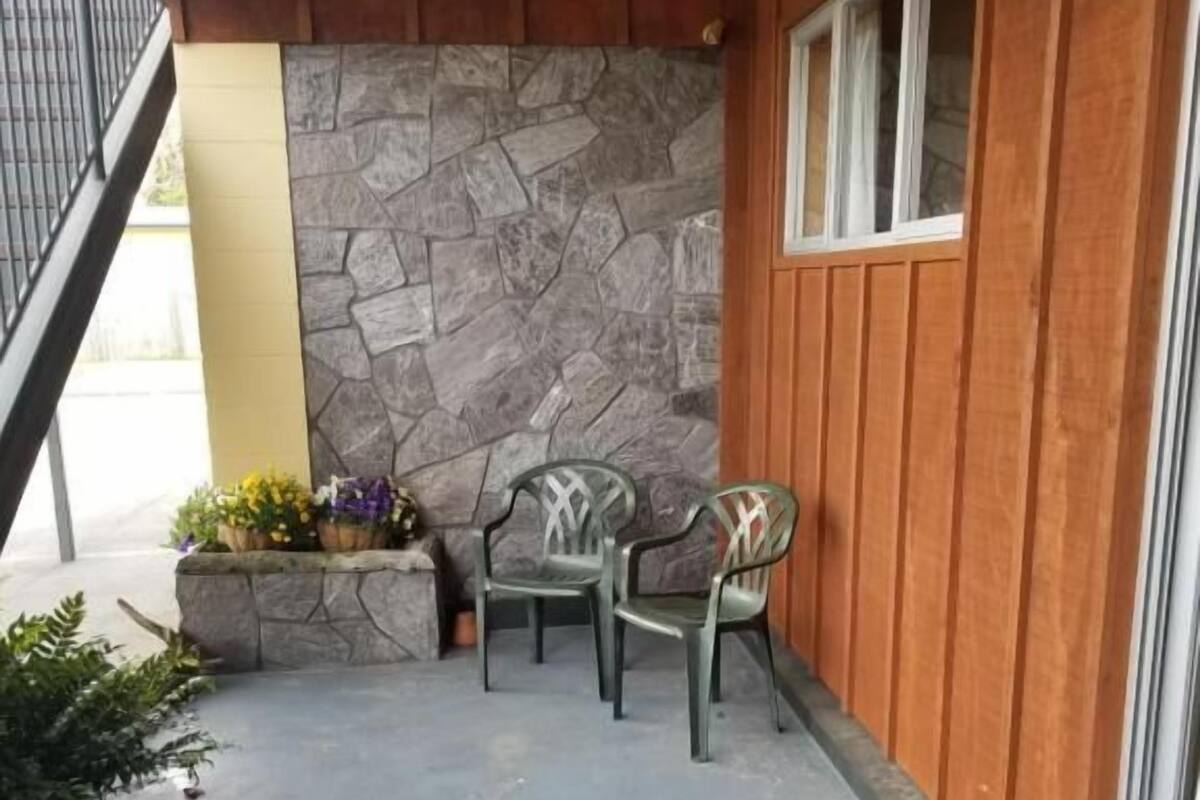 Un patio con un muro de piedra, paneles de madera y dos sillas.