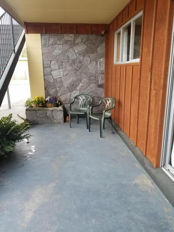 Een terras met een stenen muur, houten lambrisering en twee stoelen.
