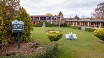 A motel named Alpine View with a well-maintained lawn, a signboard, and a building with a modern design.