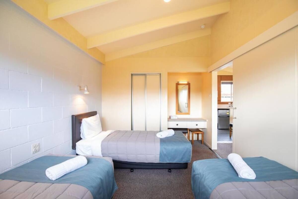 Una habitación de hotel con dos camas, un escritorio, un espejo y una kitchenette.