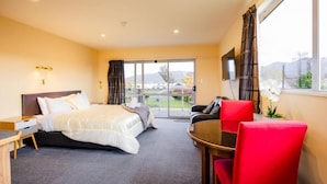 A hotel room with a bed, a desk, a chair, a TV, and a view of the outdoors.