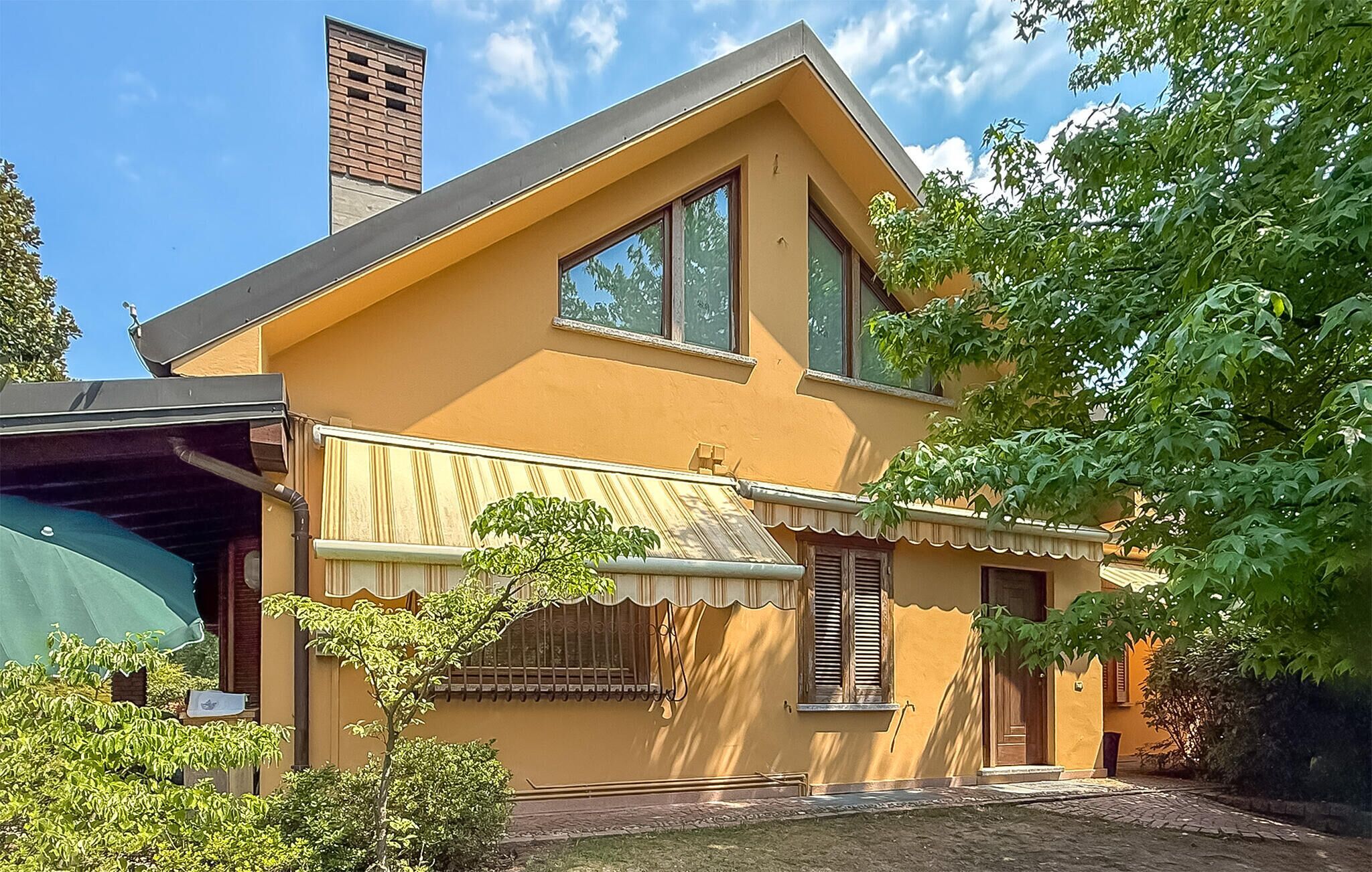 Ein zweistöckiges Haus mit geneigtem Dach, einem Schornstein und einem kleinen Vorgarten mit Baum und grünem Sonnenschirm.