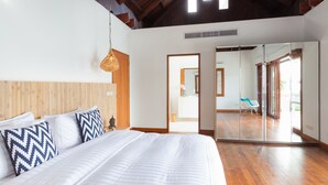 Une chambre dotée d’un grand lit, de poutres apparentes en bois au plafond, d’un luminaire suspendu et d’une porte-fenêtre coulissante donnant sur un balcon.