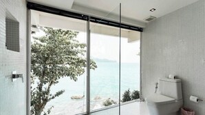 Une salle de bain moderne dotée d’une grande porte vitrée donnant sur un balcon avec vue sur la mer.