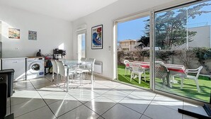 A bright kitchen with a washing machine, a glass table, and chairs, leading to a patio with a table and chairs.