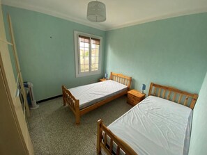 A room with two wooden beds, a window, and a ceiling light fixture. - 2-room apartment, terrace - 4 guests (Argelès-sur-Mer)