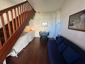 A compact living space with a wooden staircase, a dining area with a table set for four, and a sofa. - Duplex near beach and center - 3 guests (Houlgate)
