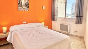 Una camera d'albergo con un letto, un comodino, una finestra con tende, un termosifone e un quadro appeso al muro.