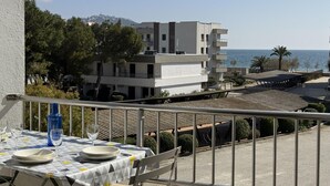 Un balcone con tavolo apparecchiato per mangiare, affacciato su una zona costiera con edifici e cielo sereno.