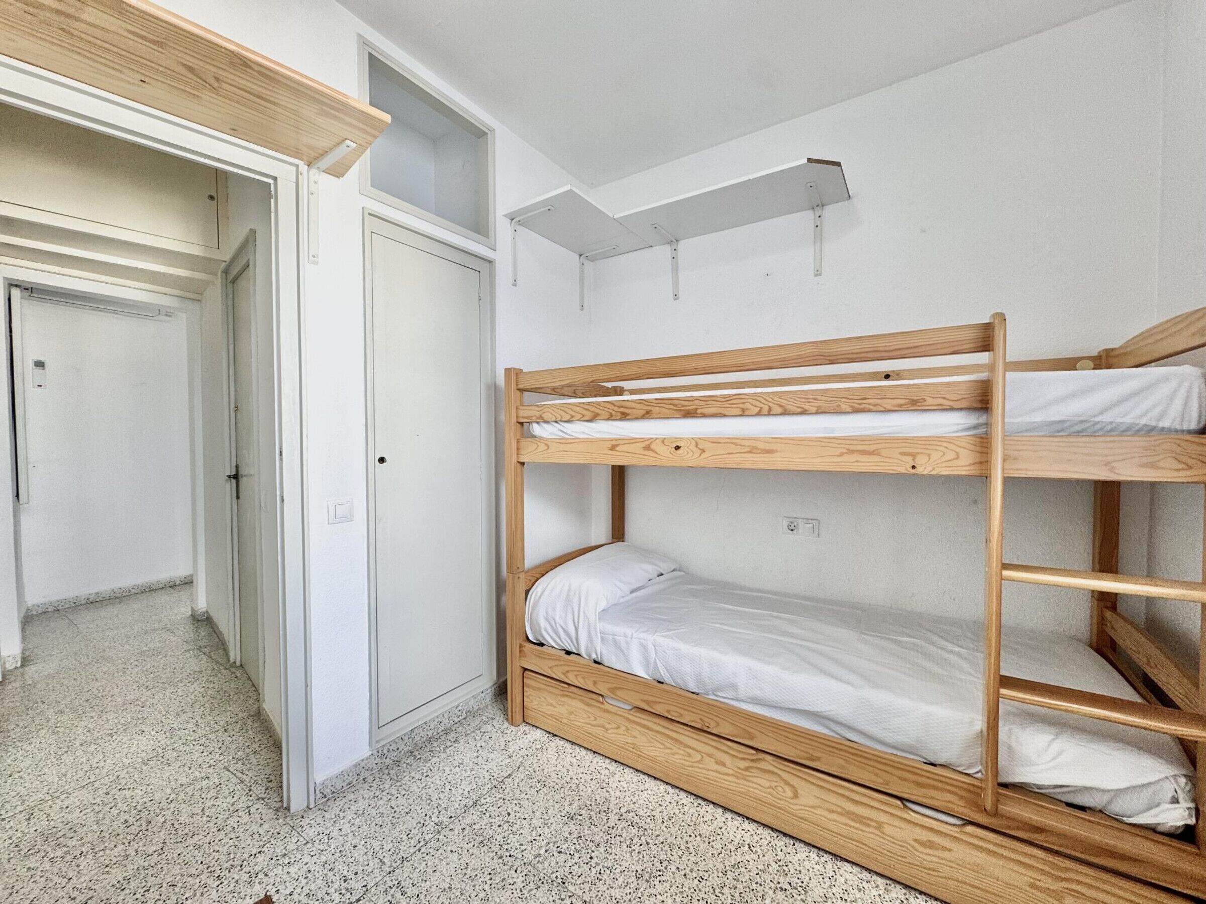 Een slaapkamer met stapelbed, een deur en een plank.