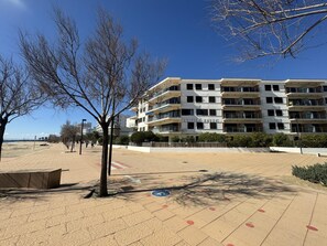 A multi-story building with balconies, a paved walkway, and trees. - 3-bedroom seafront apartment with parking in Roses (Roses)
