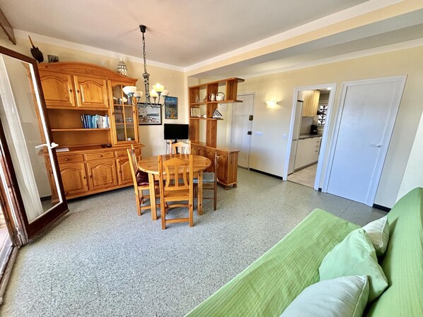 A dining area with a wooden table and chairs, a chandelier, and wooden cabinets. - 3-bedroom seafront apartment with parking in Roses (Roses)