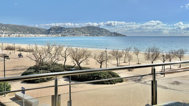 Une vue sur la côte, avec une plage, une promenade et des collines à l’horizon.