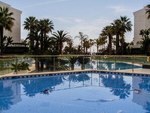 Una piscina con palmeras y baranda de cristal.