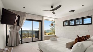 A bedroom with a bed, a TV, a ceiling fan, and a balcony with a view.