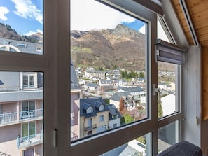 A room with a large window overlooking a town and mountains. - Charming apartment, mountain view - 4 guests (Cauterets)