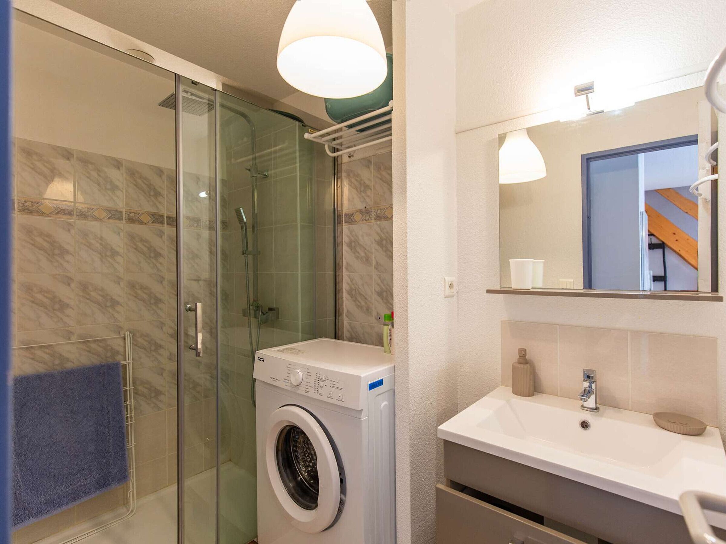 A modern bathroom with a glass shower enclosure, a built-in washing machine, and a vanity with a mirror.