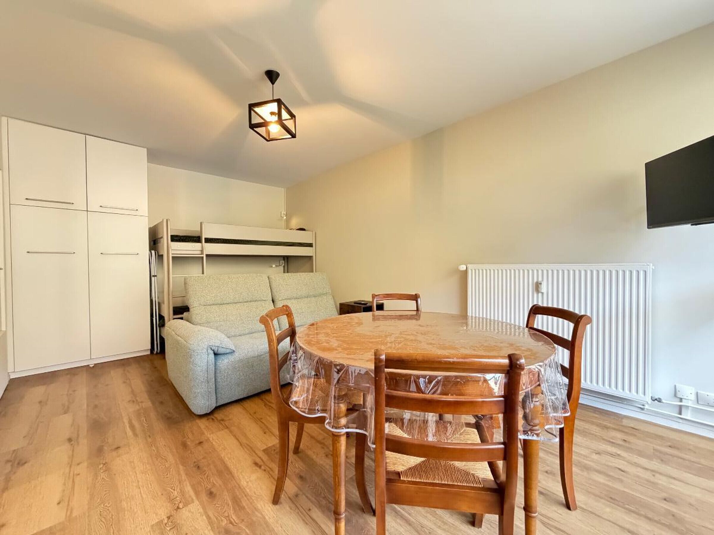 Quarto compacto com uma mesa de jantar redonda de madeira, duas cadeiras de madeira, uma cama beliche e um lustre.